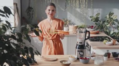 Kamerayla konuşan, havuç ve tatlı kirazları karıştıran mutlu genç bir kadının izini sürerken aynı zamanda mutfaktaki bitkilerle buzlu içecek hazırlıyor. Kadın yemek blogcusu kayıt tarifi