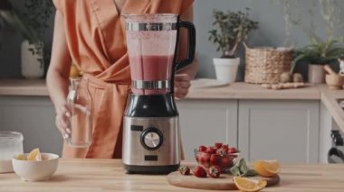 Tanımlanamayan genç bir kadının orta bölüm çekimlerinde leziz pembe smoothie 'yi mutfaktaki cam şişeye dolduruyor.