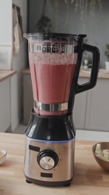 Masada duran mutfak blendırında karıştırılmış pembe smoothie 'nin el yapımı dikey görüntüsü.