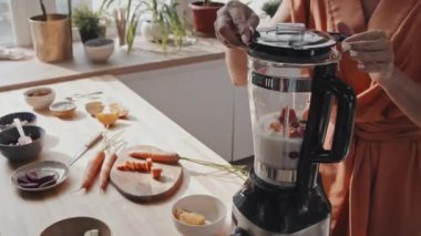 Mutfakta meyve püresi karıştıran tanınmayan genç bir kadının orta boy fotoğrafı. Mutfak tabletinde taze sebze ve meyve var.