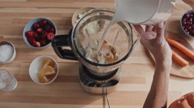 Meyveli, fındıklı ve meyveli smoothie yaparken tanınmayan genç bir kadının blender 'a süt dökerkenki görüntüsü.