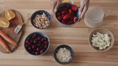 Tanınmayan genç bir kadının ahşap masaya lezzetli çilek dolu bir kâse koymasının en iyi görüntüsü. Taze sebzeler, böğürtlen, meyve, fındık ve sürahi süt masada.