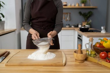 Önlüklü genç bir kadın tahtanın üzerinde süzgeçten un geçiriyor.