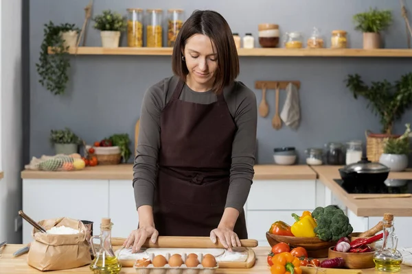 Giovane donna contemporanea rotolamento pasta fatta in casa su tavola di legno — Foto Stock