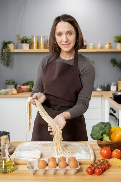 Glückliche junge Kaukasierin in Schürze beim Zubereiten von Spaghetti — Stockfoto