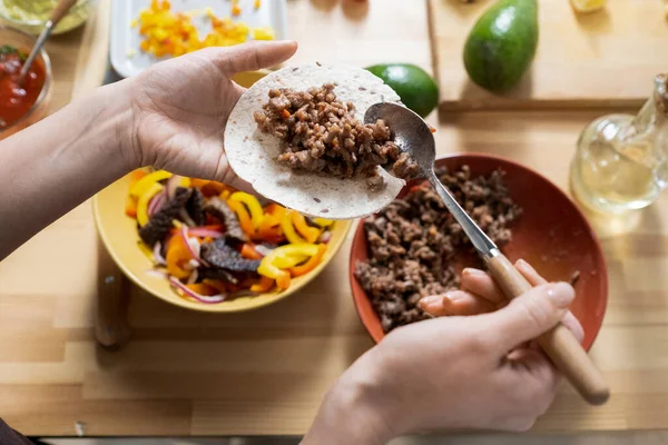 Hands of young woman with spoon putting fried minced meat on taco tortillas — Fotografia de Stock