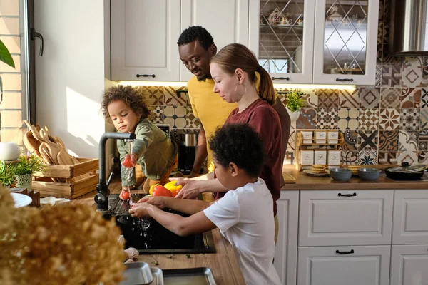 Joven familia interracial de cuatro verduras de lavado en la cocina —  Fotos de Stock