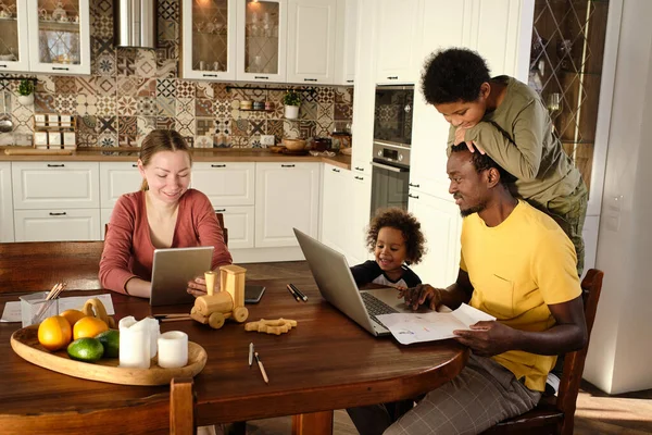 Familia contemporánea sentada junto a una mesa de madera y viendo videos en línea —  Fotos de Stock