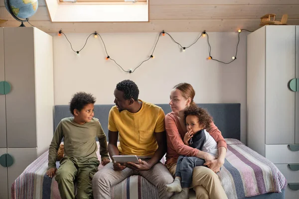 Lindo chico birracial mirando a su padre africano con la tableta mientras la familia interracial descansa en casa —  Fotos de Stock