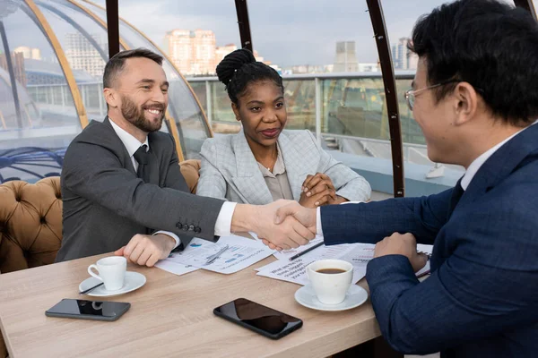 Two intercultural successful businessmen shaking hands over table — Stockfoto