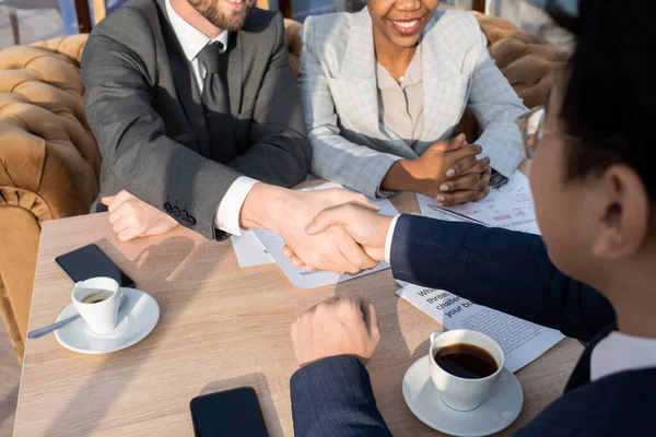Handshake of two successful business partners over table with papers and cups of coffee — Fotografia de Stock