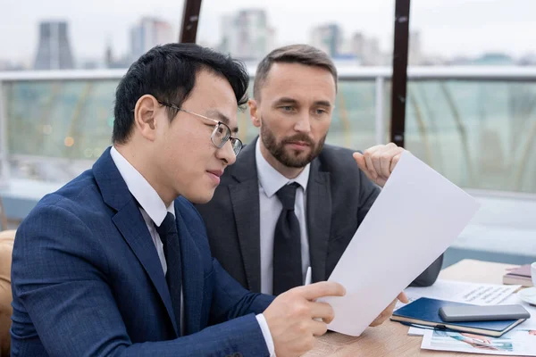 Young Chinese broker showing his Caucasian colleague new contract — Stockfoto