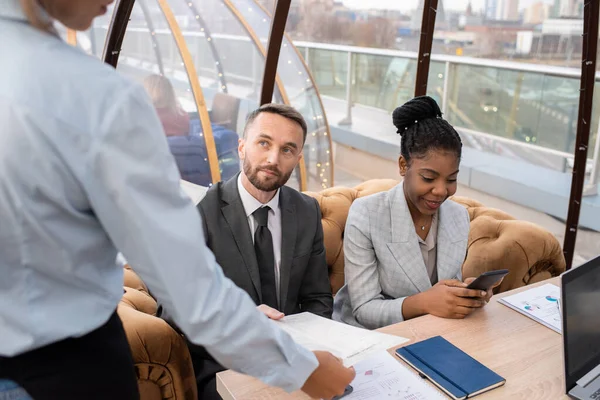 Jonge zakenman kijkt naar serveerster tijdens het doorgeven van haar menu terug — Stockfoto