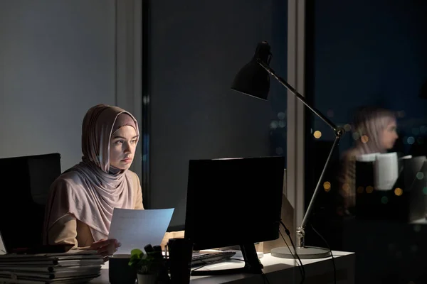 Joven musulmana en hijab sosteniendo papel y mirando la pantalla de la computadora —  Fotos de Stock