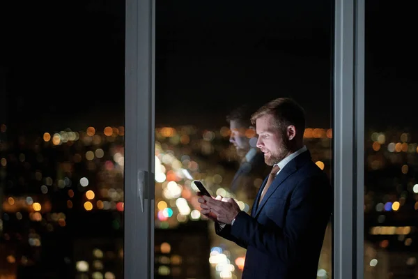 Vue latérale de l'homme d'affaires défilant dans le téléphone mobile contre une grande fenêtre — Photo