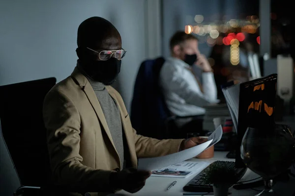 Young serious economist in protective mask looking through papers — Stock Photo, Image