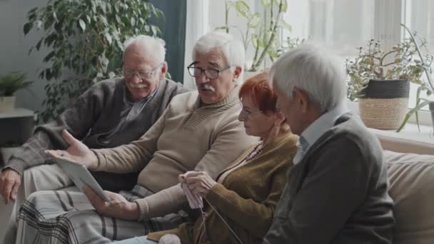 4人の高齢者がデジタルタブレットを使いながら話し合いをしながら 介護施設のソファに腰を下ろしている様子 — ストック動画