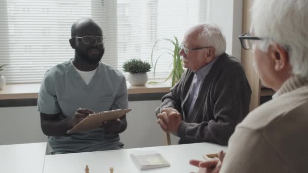 Średnie Ujęcie Afrykańsko Amerykańskiej Pielęgniarki Dwóch Starszych Mężczyzn Rozmawiających Przy — Wideo stockowe