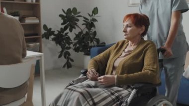 Tanımlanamayan hemşire ya da sosyal hizmet görevlisinin yaşlı üzgün bir kadınla huzurevinde yürümesi.