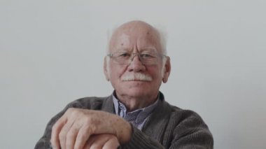 Gözlüklü, gri bıyıklı, beyaz arka planda oturan ve kameraya bakan Kafkasyalı son sınıf öğrencisinin portresini kapat.