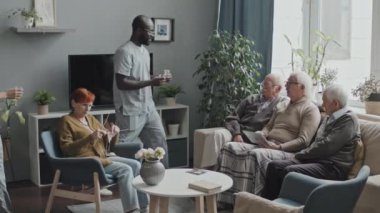 Çok ırklı hemşireler, huzurevinin oturma odasında boş vakitlerini televizyon izleyerek geçiren yaşlılar için tek kullanımlık bardaklar ve haplar getiriyor.