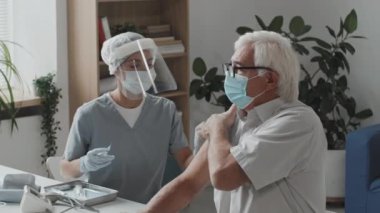Kafkas maskeli üst düzey bir adamın koronavirüse karşı koruyucu yüz maskesi takan genç bir kadın doktor tarafından aşılandığı orta boy bir fotoğraf.