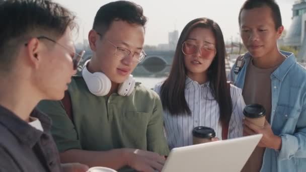 夏の日に川の堤防に立ってノートパソコンの画面を見ている間に話している4人のアジアの同僚や友人のチームの中ショット — ストック動画