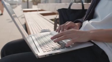 Uzaktan kumandalı işçilerin, dışarıda bankta oturup dizüstü bilgisayarda yazı yazarken tanınmayan ellerini kapatın.