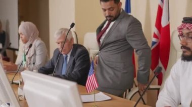 Orta Doğu ülkesinden erkek politikacının çok ırklı siyasi liderlerle basın toplantısına geldiği ve mikrofonla izleyicilere seslendiği orta boy bir fotoğraf.