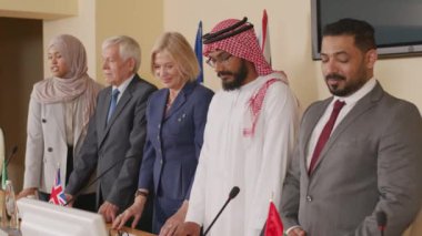 Üç yabancı erkek ve iki kadın politikacının basın toplantısında fotoğraflandıktan sonra masada oturdukları orta boy fotoğraf.