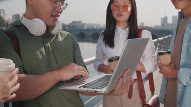 夏に屋外で働く4人の若いアジア人の同僚の中程度のショット ラップトップで川の堤防に立って — ストック動画