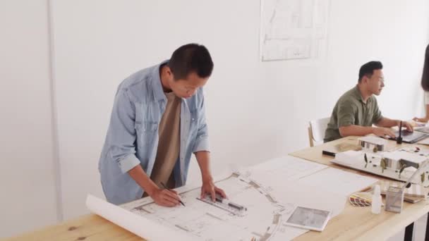 背景にあるプロジェクトの詳細を議論しながら 彼の同僚はプロのアジアの男性建築家の図面の家の計画の中のショット — ストック動画