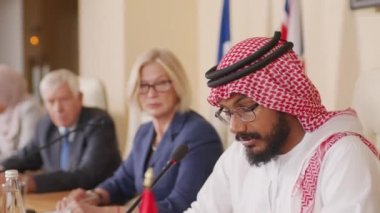 Arap dışişleri bakanının geleneksel kıyafet hazırlama konuşmasında orta ölçekli bir şekilde diğer dört ülkenin siyasi temsilcileriyle birlikte uzun masada oturması.