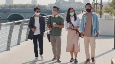 Güneşli bir günde kahve eşliğinde nehir kenarında gezinirken maskeli dört Asyalı arkadaşın yüz maskeli görüntülerini izliyoruz.