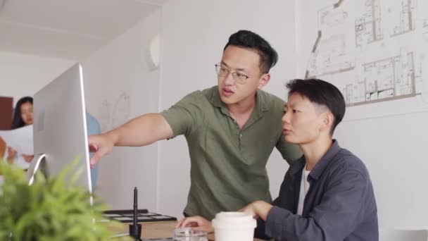 コンピュータモニタ上でプロジェクトを議論する若い創造的なアジアの建築家のチームの中のショットは 現代のオフィスで一緒に働く — ストック動画