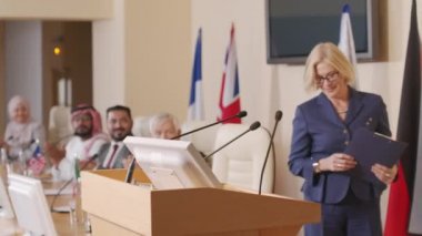 Beyaz ırkın orta yaşlı kadın siyasi liderinin resmi basın konferansında yaptığı konuşma için Tribün 'e gidişinin orta boy fotoğrafı.