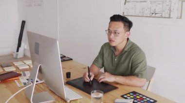 Bilgisayarda grafik tablet kullanarak ev çizimleri çizen konsantre genç erkek Asyalı mimar.