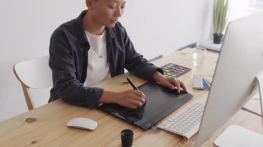 Stylus 'un bilgisayar monitörüne bakıp iş yerinde masa başında oturduğu orta boy Asyalı grafik tasarımcı resimleri.
