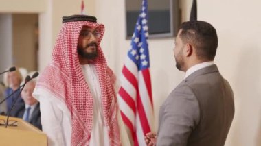 Orta halli başarılı Orta Doğu ve Arap siyasi liderlerin basın toplantısında tribünün yanında el sıkışırken çekilmiş orta ölçekli bir fotoğrafı. Diğer politikacılar arka planda alkışlıyorlar