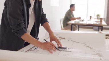 Genç Asyalı kadın mimar kalem ve cetvelle modern mimarlık ofisinde masa başında ev planı çiziyor.