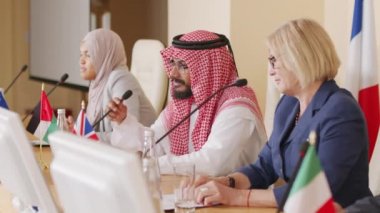 Farklı ülkelerden üç erkek ve kadın çok ırklı siyasi liderin basın toplantısı sırasında mikrofonlarla donatılmış bir masada otururken tartıştıkları orta boy bir çekim.