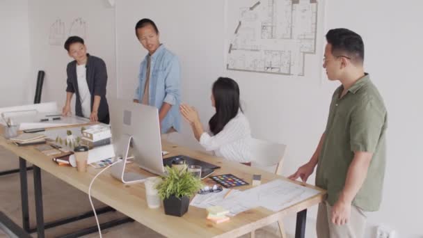 プロの建築家の陽気な若いアジアのチームは 近代的なオフィスで協力しながら 住宅プロジェクトの成功を祝うために互いに5を与えます — ストック動画