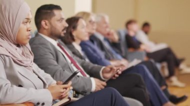 Çeşitli erkek ve kadın iş adamları ve siyasi liderlerin konferans veya konferans konuşmalarını dinleyip konferans salonunda sıra sıra oturdukları PAN çekimleri