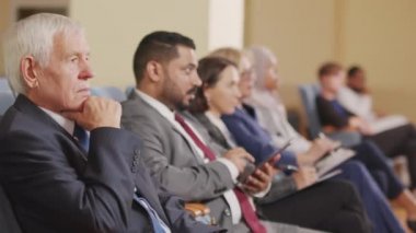 Kafkasyalı kıdemli adam ve farklı ülkelerden diğer siyasi liderlerin konferansta konuşmacıları dinlerken, büyük konferans salonunda sırada otururken PAN çekimi.