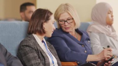 İki iş kadınının halka açık konferans ya da konferans sırasında konuştuğu orta ölçekli bir fotoğraf.