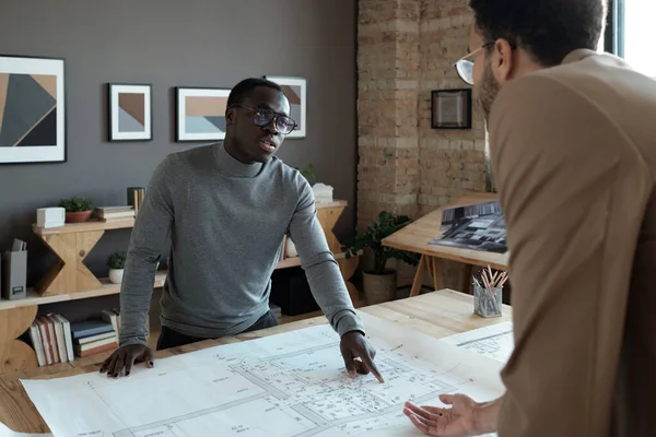 Young contemporary architect explaining details of sketch to male colleague — Stock Photo, Image