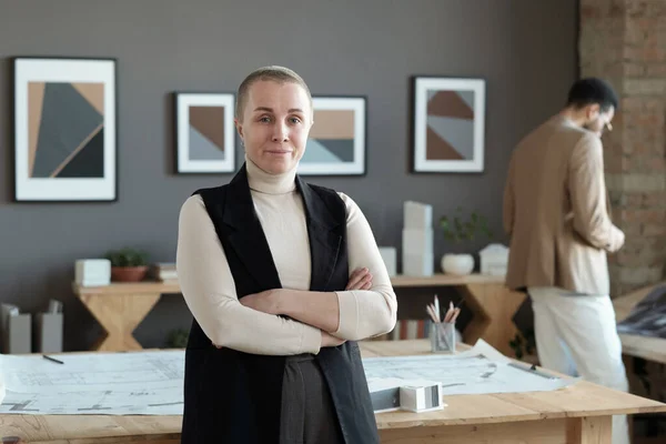 Erfolgreiche Architektin kreuzt Arme an Brust, während sie am Tisch steht — Stockfoto