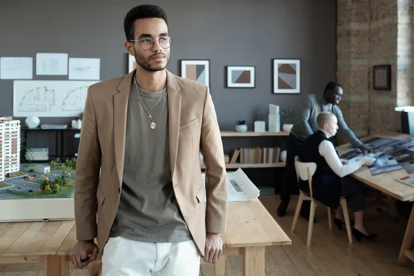 Jonge serieuze zakenman in slim casualwear stand by houten tafel — Stockfoto