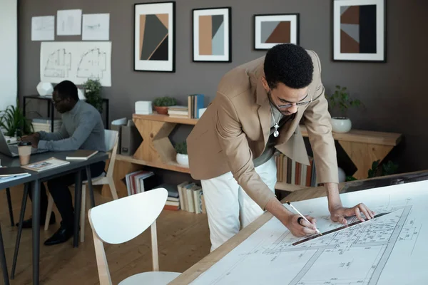 Young architect drawing line on sketch while bending over workplace — Foto de Stock
