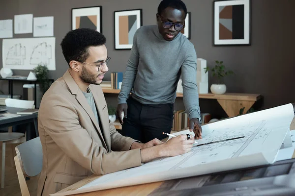 Two young intercultural businessmen discussing sketch of architecture on blueprint — Foto de Stock